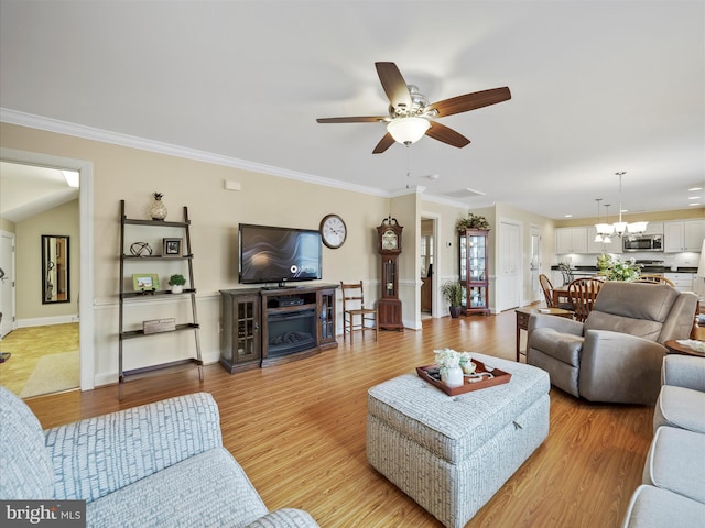 living area with ornamental molding, light wood finished floors, ceiling fan with notable chandelier, and baseboards