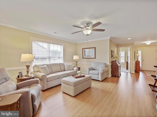 living area featuring light wood-style floors, ceiling fan, visible vents, and ornamental molding