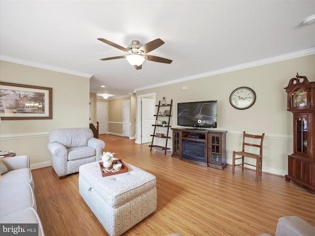 living room with ceiling fan, a fireplace, wood finished floors, baseboards, and crown molding