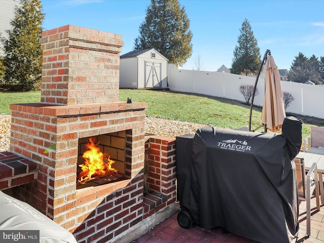 view of patio / terrace featuring a fenced backyard, an outdoor structure, a grill, an outdoor brick fireplace, and a shed