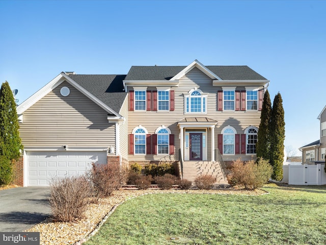 colonial house with a shingled roof, a front yard, driveway, and fence