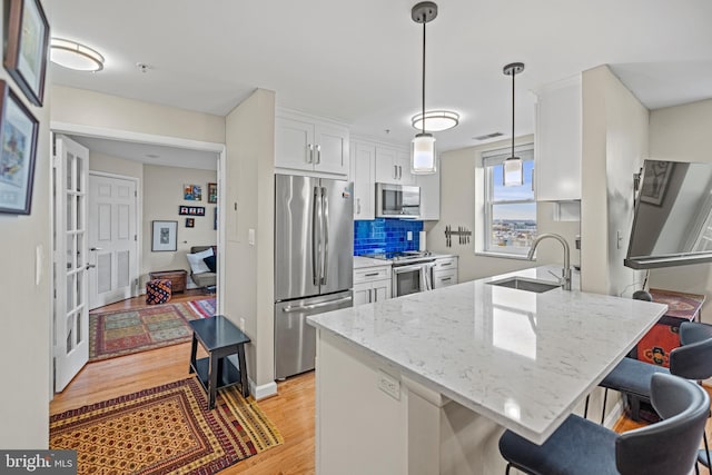 kitchen featuring appliances with stainless steel finishes, light wood-style floors, white cabinetry, a sink, and a peninsula