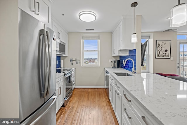 kitchen featuring stainless steel appliances, backsplash, light wood-style flooring, white cabinetry, and a sink