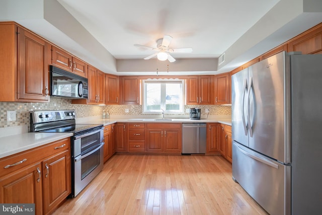 kitchen featuring a sink, light wood-style floors, appliances with stainless steel finishes, brown cabinetry, and light countertops