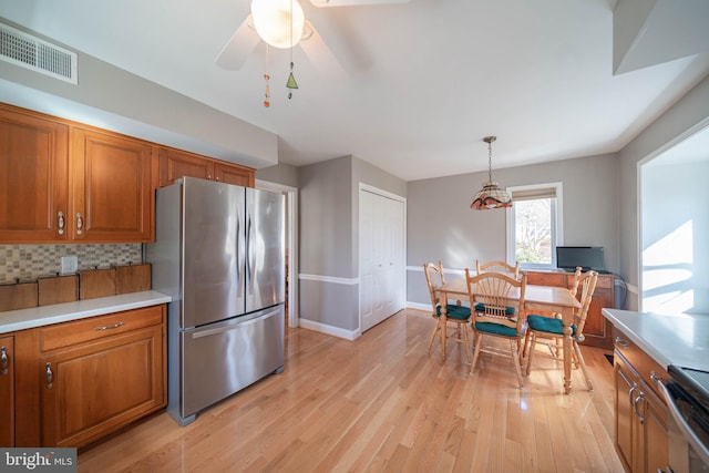 kitchen with brown cabinetry, visible vents, light wood finished floors, stainless steel appliances, and tasteful backsplash