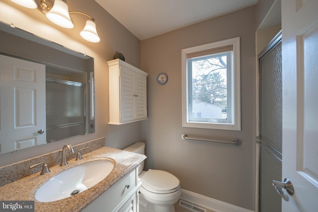 bathroom featuring vanity, baseboards, visible vents, toilet, and a shower with door