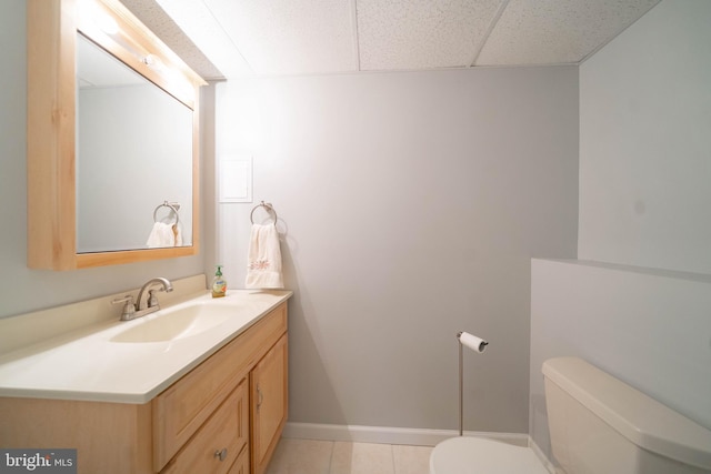 bathroom with toilet, tile patterned flooring, a paneled ceiling, baseboards, and vanity