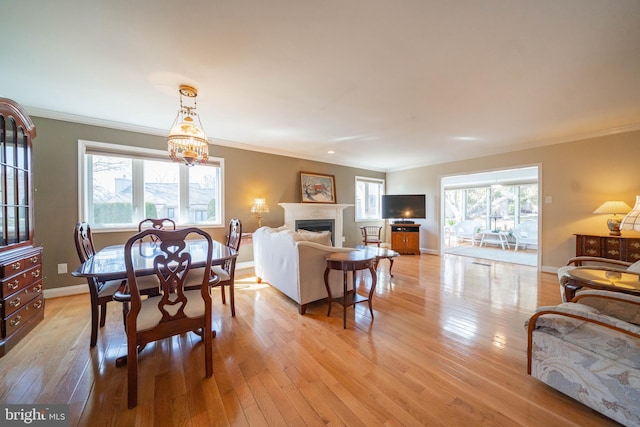 dining space featuring a fireplace, light wood-type flooring, baseboards, and ornamental molding