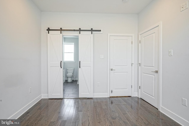 unfurnished bedroom with a barn door, connected bathroom, baseboards, and wood finished floors