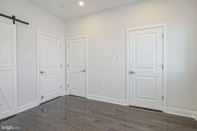 unfurnished bedroom with a barn door, baseboards, dark wood-style flooring, and recessed lighting