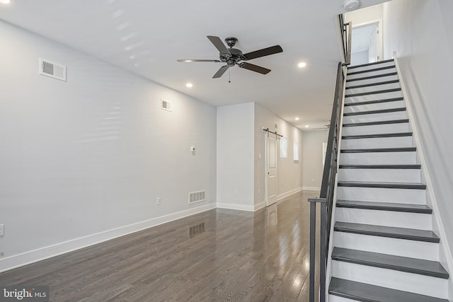 staircase with a barn door, visible vents, ceiling fan, and wood finished floors