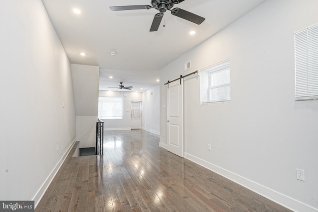 unfurnished living room with a barn door, visible vents, baseboards, wood-type flooring, and recessed lighting