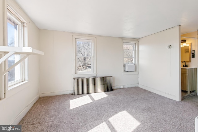 carpeted spare room with radiator, a sink, cooling unit, and a wealth of natural light