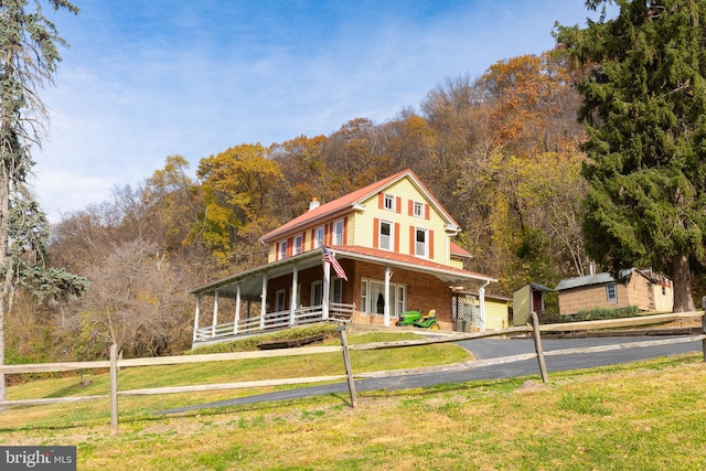 farmhouse with covered porch, brick siding, a front lawn, and a view of trees