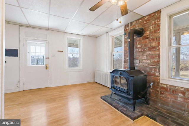 foyer entrance with a ceiling fan, radiator, wood finished floors, a wood stove, and a paneled ceiling