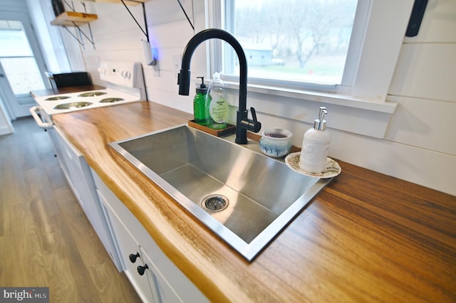 interior details with a sink, white electric range oven, wood finished floors, white cabinetry, and open shelves