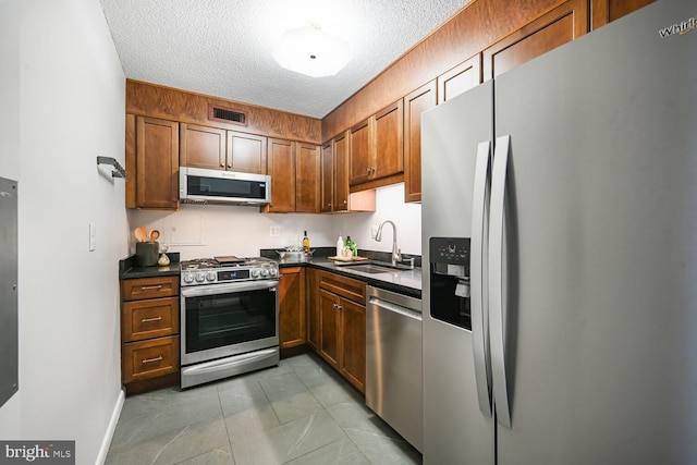 kitchen featuring dark countertops, visible vents, appliances with stainless steel finishes, a textured ceiling, and a sink