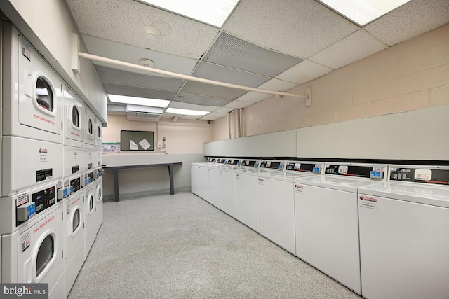 shared laundry area featuring washer and dryer, concrete block wall, and stacked washing maching and dryer