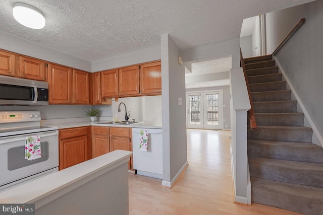 kitchen with a sink, a textured ceiling, white appliances, light wood-style floors, and light countertops