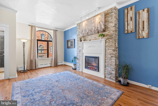 unfurnished living room with baseboards, a glass covered fireplace, ornamental molding, wood finished floors, and a baseboard heating unit