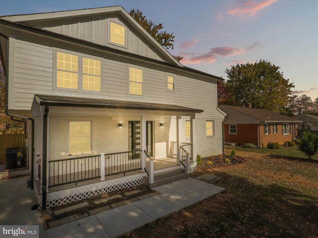 view of front of property with cooling unit, a porch, board and batten siding, and brick siding