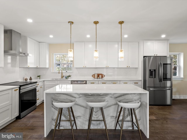 kitchen featuring stainless steel appliances, a sink, wall chimney range hood, and a breakfast bar area