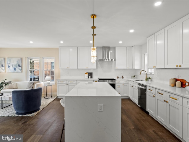 kitchen with dark wood-style floors, appliances with stainless steel finishes, a sink, wall chimney range hood, and a kitchen island