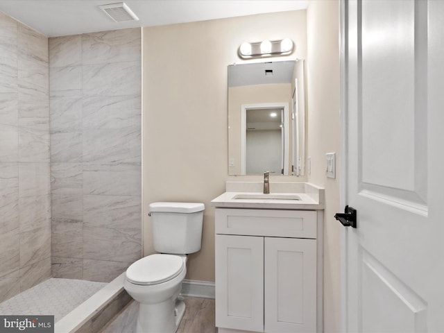 full bath with baseboards, visible vents, toilet, a tile shower, and vanity