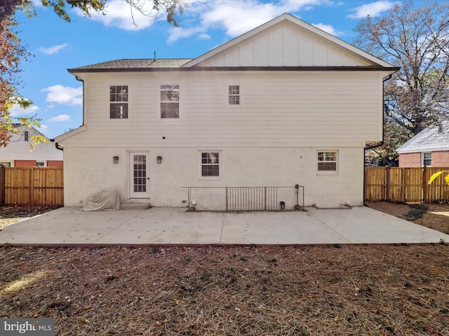 rear view of property with board and batten siding, a patio area, brick siding, and fence