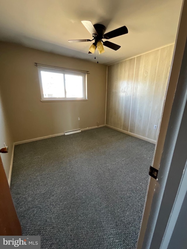 carpeted spare room featuring a baseboard heating unit, baseboards, wooden walls, and a ceiling fan