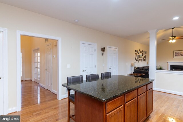 kitchen featuring a fireplace, light wood finished floors, baseboards, brown cabinetry, and a kitchen bar