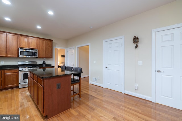 kitchen with appliances with stainless steel finishes, a center island, light wood finished floors, brown cabinetry, and a kitchen bar