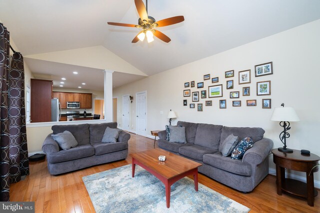 living room featuring a ceiling fan, baseboards, vaulted ceiling, light wood finished floors, and ornate columns