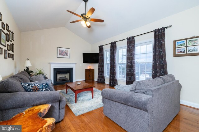 living area featuring lofted ceiling, a fireplace, wood finished floors, and baseboards