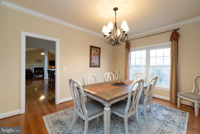 dining space featuring a fireplace, baseboards, crown molding, and wood finished floors