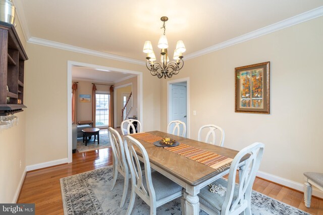 dining room featuring crown molding, light wood finished floors, baseboards, and a notable chandelier