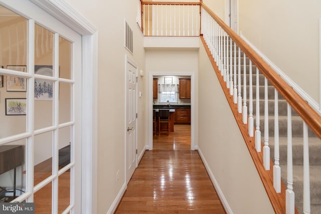 interior space featuring visible vents, baseboards, a towering ceiling, wood-type flooring, and stairway