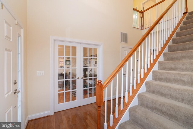 staircase with baseboards, visible vents, wood finished floors, a high ceiling, and french doors