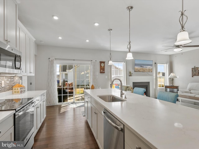 kitchen featuring backsplash, light countertops, a fireplace, stainless steel appliances, and a sink