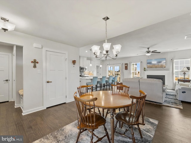 dining space featuring visible vents, baseboards, ceiling fan with notable chandelier, a fireplace, and dark wood-style flooring