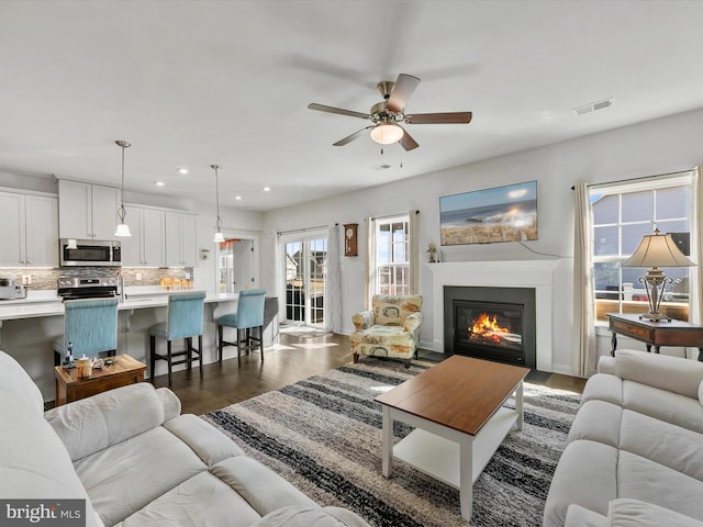 living area featuring visible vents, a ceiling fan, a glass covered fireplace, recessed lighting, and dark wood-style flooring