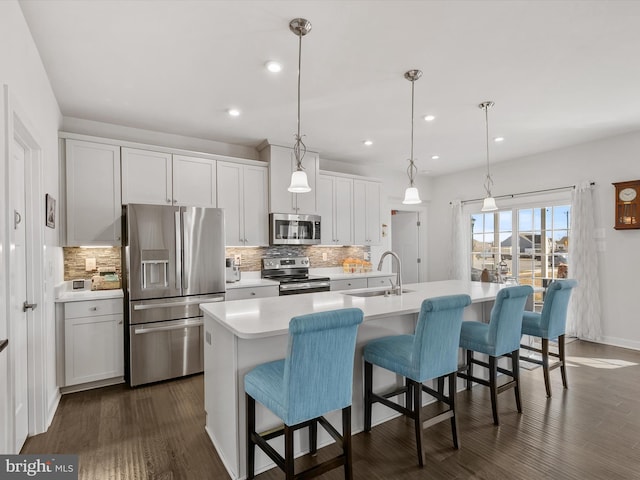 kitchen featuring dark wood finished floors, a breakfast bar area, light countertops, stainless steel appliances, and a sink