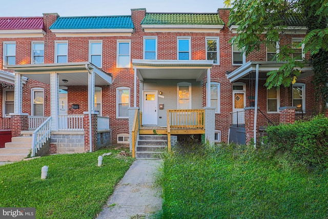 townhome / multi-family property with a porch, brick siding, and mansard roof