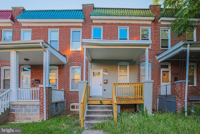 view of property featuring a tiled roof, mansard roof, a porch, and brick siding