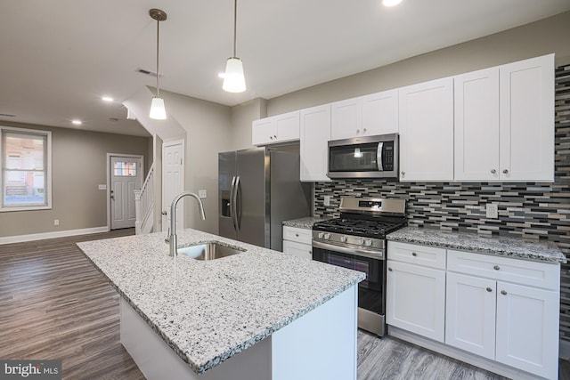 kitchen featuring a kitchen island with sink, a sink, white cabinets, appliances with stainless steel finishes, and tasteful backsplash