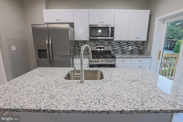 kitchen featuring light stone counters, stainless steel appliances, a sink, decorative backsplash, and a center island with sink