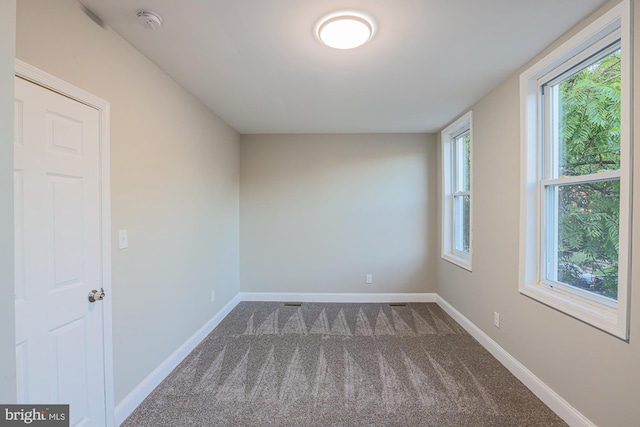 empty room with baseboards and dark colored carpet