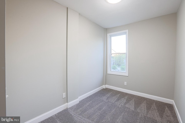 unfurnished room with baseboards and dark carpet