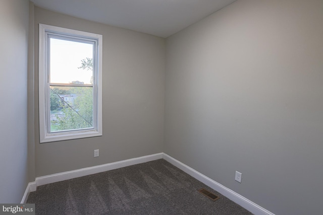 empty room featuring baseboards, visible vents, and dark carpet