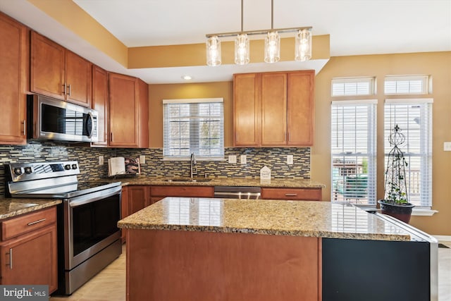 kitchen featuring a sink, a kitchen island, tasteful backsplash, appliances with stainless steel finishes, and light stone countertops